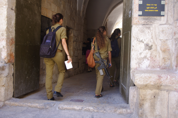 Israeli Soldaten in Uniform gehen durch einen Torbogen im Alten Stadt Jerusalem, einer hält eine Waffe und ein Blatt Papier, mit einer Tafel an der Wand rechts.