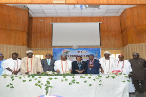 Gruppe von Menschen, die um einen mit einer weißen Decke und Blumen und Blättern geschmückten Tisch auf der ICCI International Trade Fair 2019 stehen, mit einem Banner, einem Projektionsschirm und Deckenleuchten im Hintergrund.